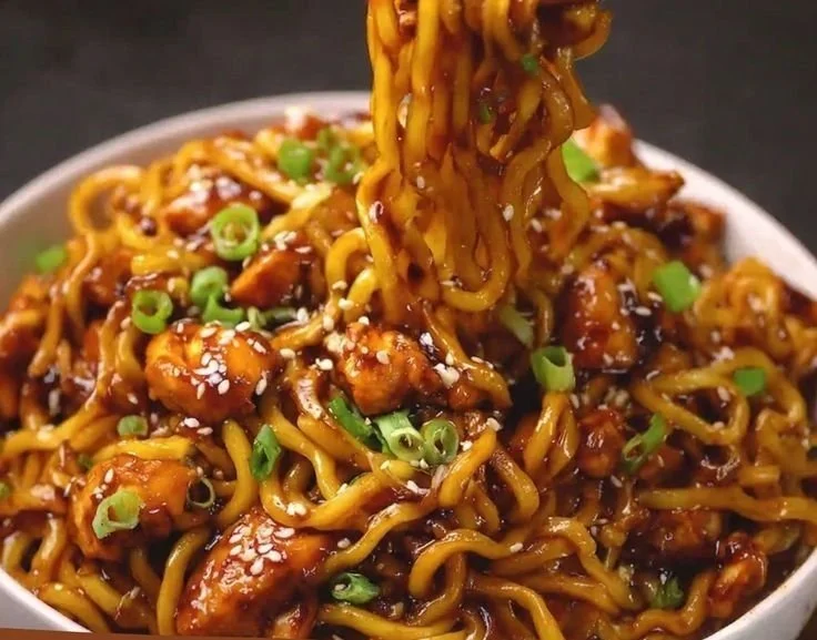 Plate of sticky garlic chicken noodles garnished with herbs