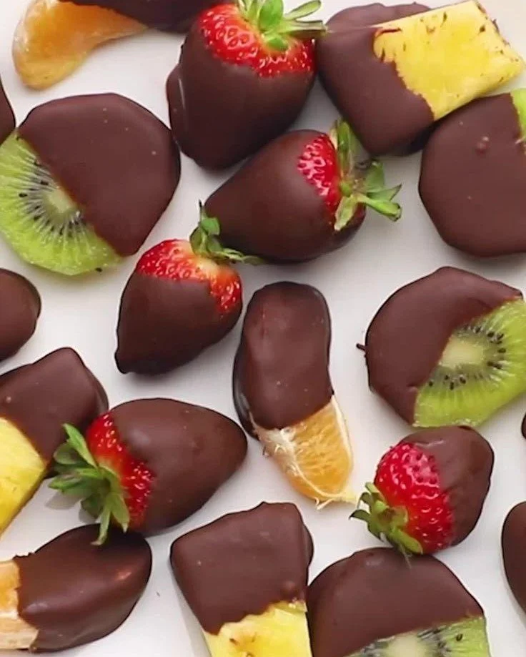 Various chocolate-dipped fruits on a white plate, including strawberries and bananas.