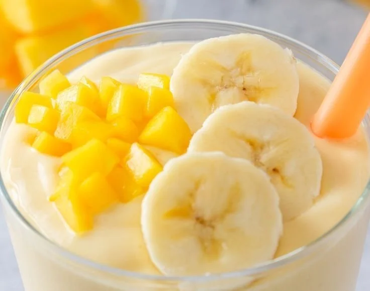 Extra creamy mango banana smoothie in a glass garnished with fresh fruit