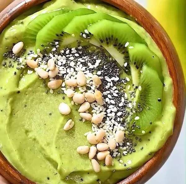 Green matcha smoothie bowl topped with fruits and nuts