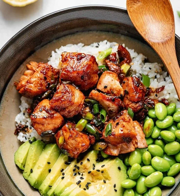 Teriyaki salmon bowl with fresh vegetables and rice, topped with sesame seeds.