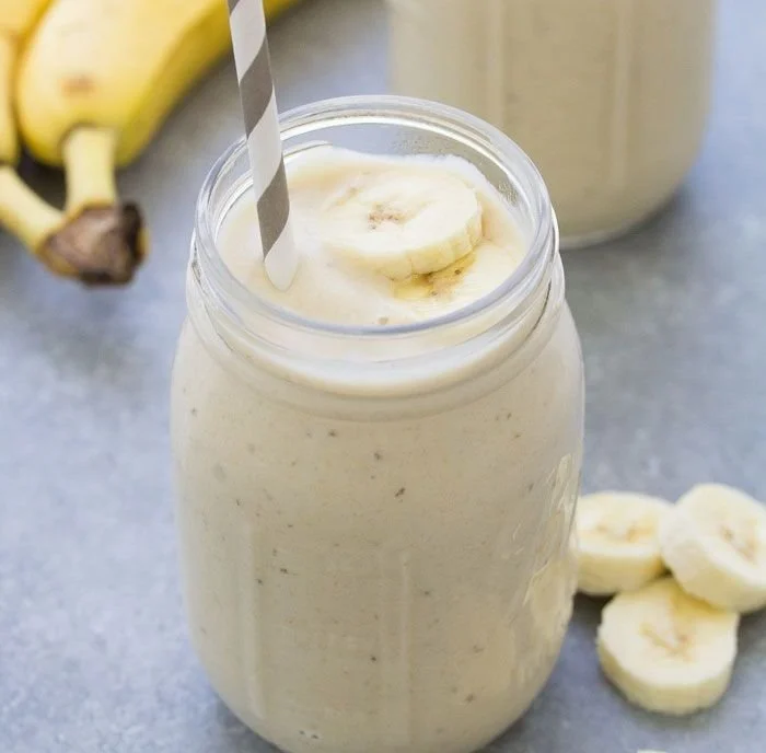 Creamy healthy banana smoothie in a glass with fresh bananas and mint leaves.